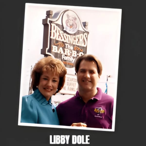 Libby Dole and a man smiling in front of the Bessinger's BBQ sign.