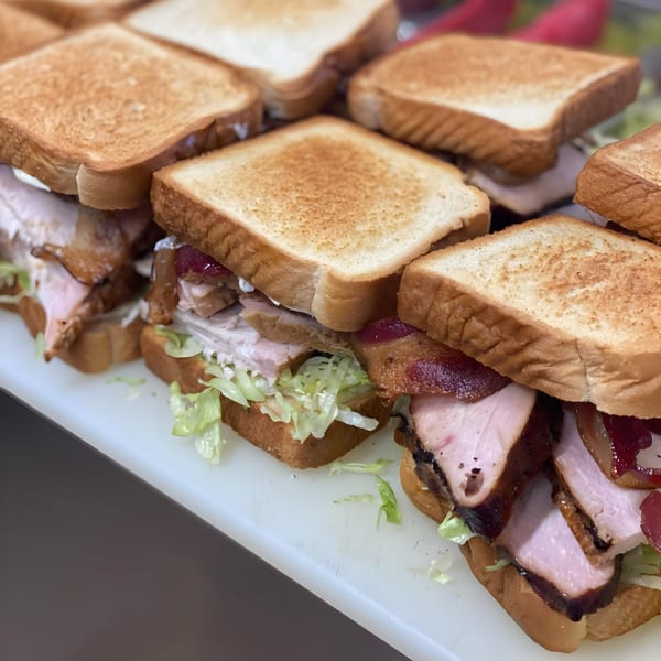 Several Bessinger's BBQ sandwiches with sliced meat, lettuce, and toasted bread on a white surface.