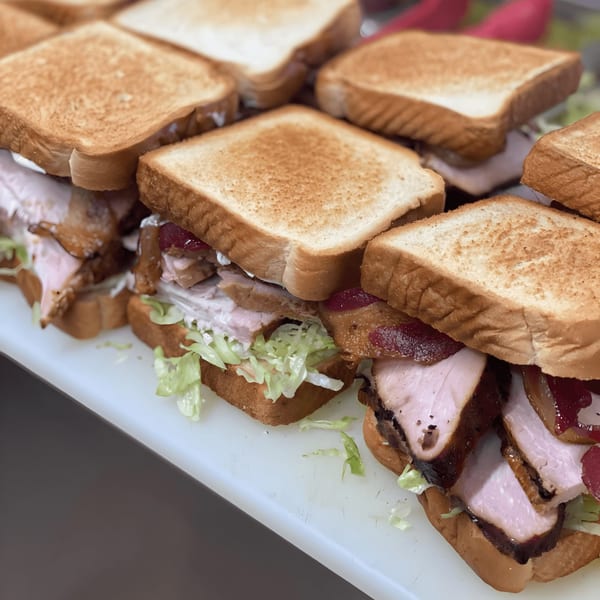 Multiple Bessinger's BBQ turkey sandwiches with lettuce and cranberry sauce on toasted bread.