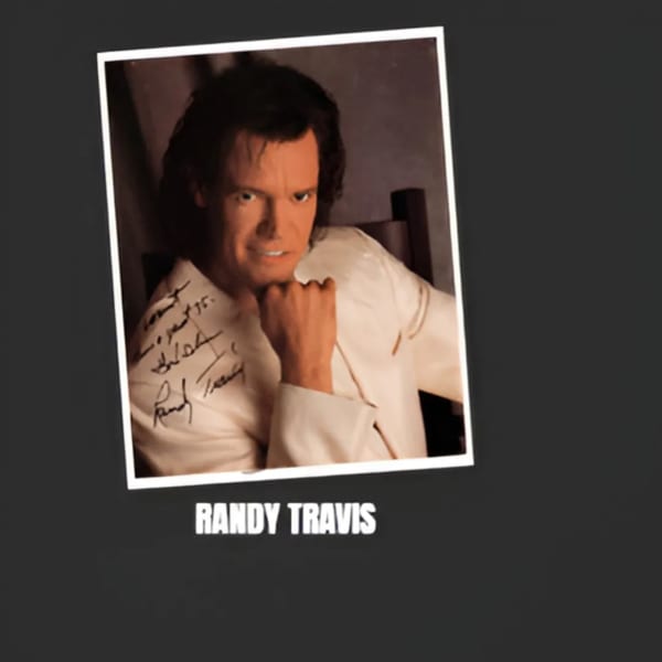 Randy Travis in a white jacket with an autograph, featured in a framed photo.