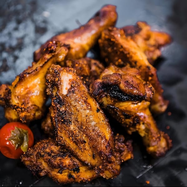 A close-up of several golden-brown, seasoned BBQ chicken wings with a small red pepper.