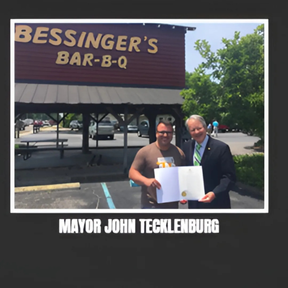 Two men, one in a suit, holding a document in front of Bessinger's BBQ restaurant.