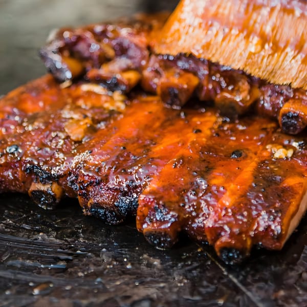 Bessinger's BBQ ribs being brushed with a rich, glossy barbecue sauce.