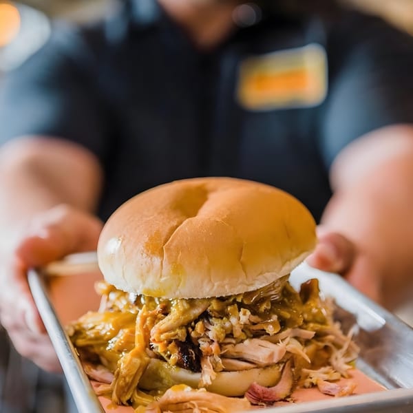 A server presents a Bessinger's BBQ pulled pork sandwich on a metal tray.