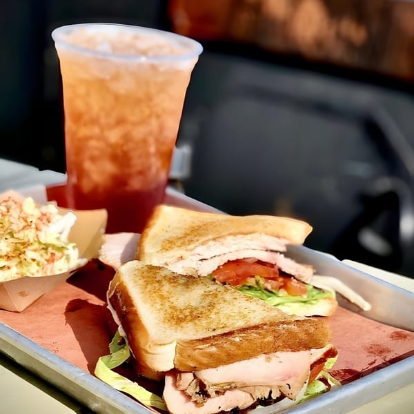 Bessinger's BBQ turkey sandwich with coleslaw and iced tea on a metal tray.