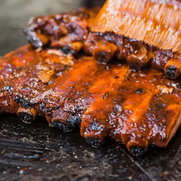 Bessinger's BBQ ribs being brushed with a rich, glossy barbecue sauce.