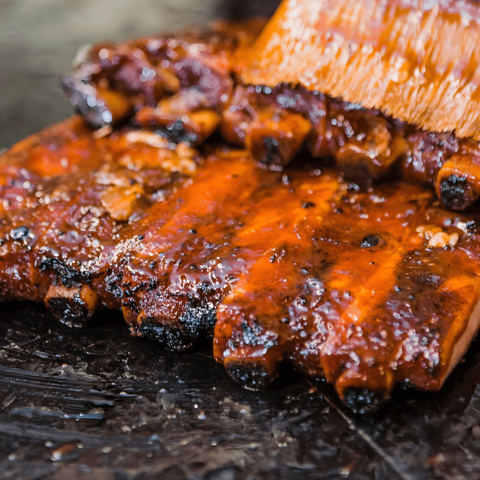 Bessinger's BBQ ribs being brushed with a rich, glossy barbecue sauce.